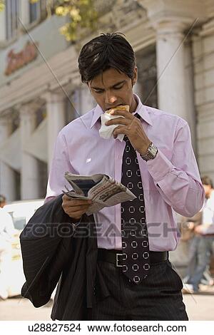 Picture - Man eating while reading a newspaper. Fotosearch