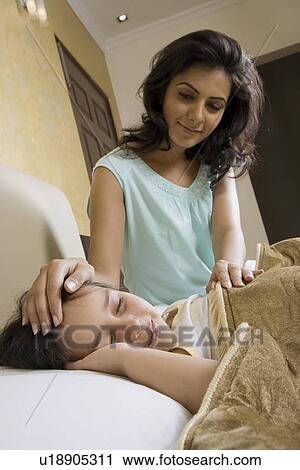 Stock Image - Mother putting her daughter to sleep. Fotosearch