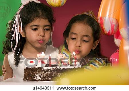 Stock Image - Two girls blowing candles. Fotosearch