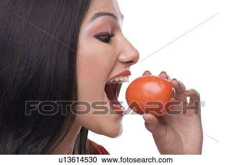 Stock Image - Woman about to eat a tomato. Fotosearch