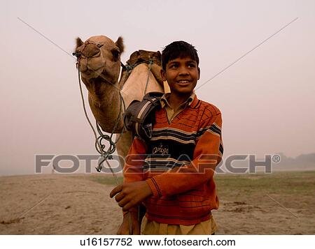 Stock Image - Boy standing with a camel in India. Fotosearch