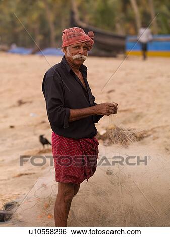 Stock Photograph - Fisherman untangling net on beach. Fotosearch