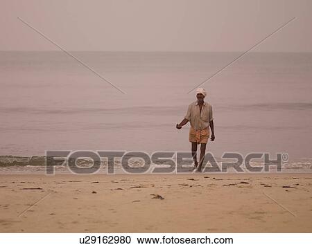 Stock Image - Man walking on beach of Arabian Sea. Fotosearch