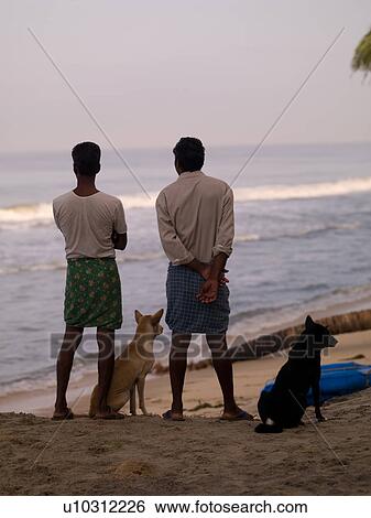 Stock Photograph - Men and their dogs on the Arabian Sea beach. Fotosearch