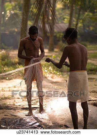 Stock Image - Men opening fish nets on shore of Arabian Sea. Fotosearch