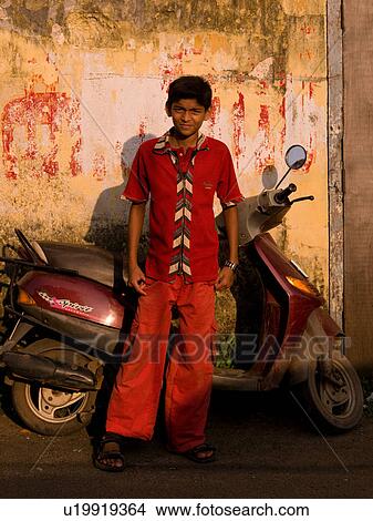 Picture - Teenage boy standing in front of a scooter in India. Fotosearch