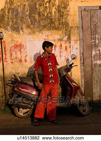 Stock Image - Teenage boy standing in front of a scooter in India. Fotosearch