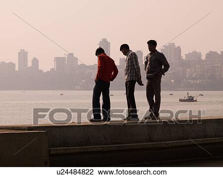 "Three men standing beside water, city in background" View Large Photo Image Stock Image - "Three men standing beside water, city in background". Fotosearch