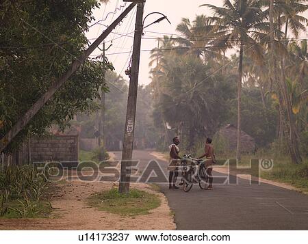 Stock Photo - Two men with bikes on roadway in Kerala India. Fotosearch