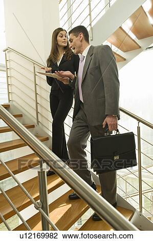 Stock Image - Businessman and businesswoman on staircase arguing over document. Fotosearch