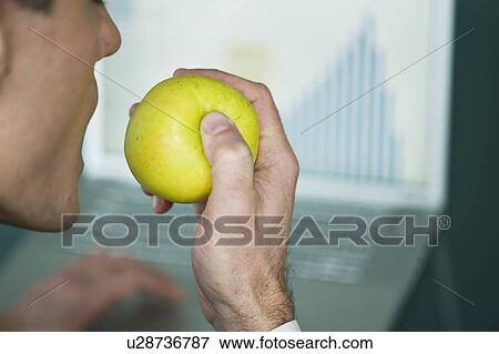 Stock Photo - Businessman eating apple at laptop with bar chart. Fotosearch