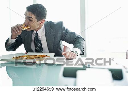 Stock Photo - Businessman eating pizza at desk. Fotosearch