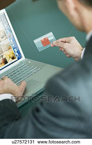 Stock Image - Businessman holding credit card at laptop. Fotosearch