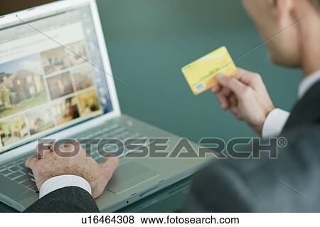 Businessman holding credit card at laptop View Large Photo Image Stock Photo - Businessman holding credit card at laptop. Fotosearch