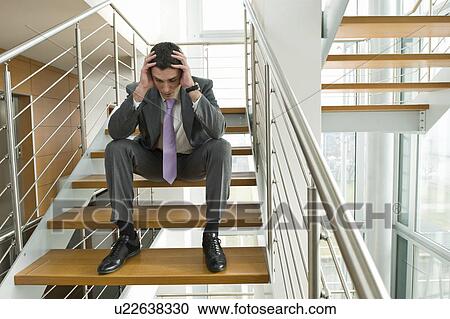 Stock Image - Businessman on office staircase with head in hands. Fotosearch