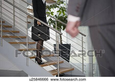 Stock Photograph - Businessman walking up to businesswoman on staircase. Fotosearch