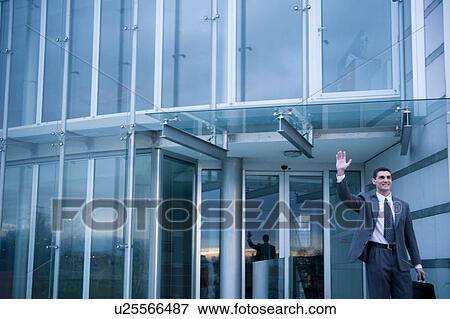 Stock Photo - Businessman waving while exiting from office building. Fotosearch