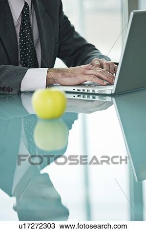 Stock Image - Businessman with apple at laptop. Fotosearch