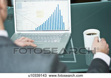 Stock Image - Businessman with coffee cup at laptop with bar chart. Fotosearch