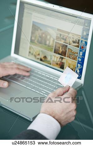 Stock Image - Businessman's hands holding credit card at laptop. Fotosearch