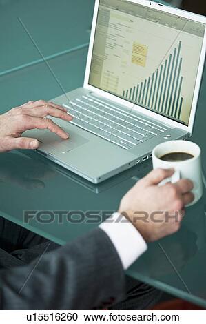 Stock Image - Businessman's hands with coffee cup at laptop with bar chart. Fotosearch