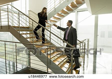 Stock Photo - Businesswoman and businessman exchanging document on office staircase. Fotosearch