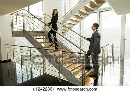 Stock Photo - Businesswoman and businessman walking up office staircase. Fotosearch