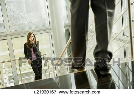 Businesswoman on cell phone and businessman walking down staircase View Large Photo Image Stock Photo - Businesswoman on cell phone and businessman walking down staircase. Fotosearch
