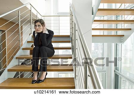Stock Image - Businesswoman on office staircase holding her head. Fotosearch