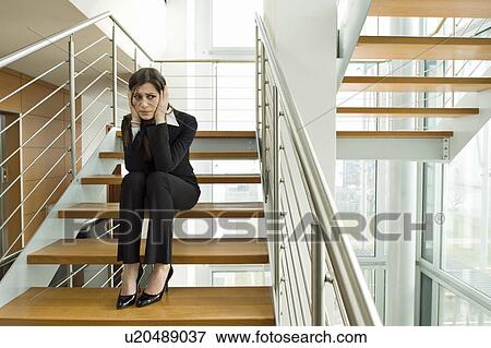 Stock Photo - Businesswoman on office staircase holding her head. Fotosearch