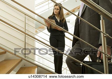 Picture - Businesswoman on staircase reading document and businessman walking up. Fotosearch
