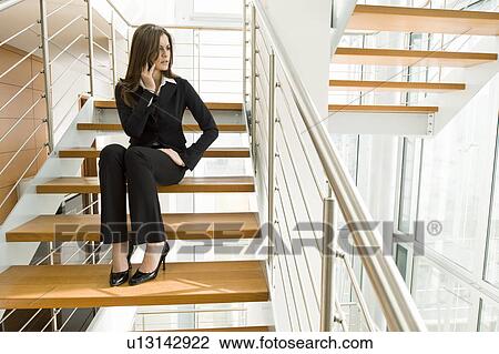 Stock Image - Businesswoman talking on cell phone on office staircase. Fotosearch