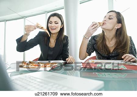 Businesswomen eating pizza at desk View Large Photo Image Stock Photo - Businesswomen eating pizza at desk. Fotosearch