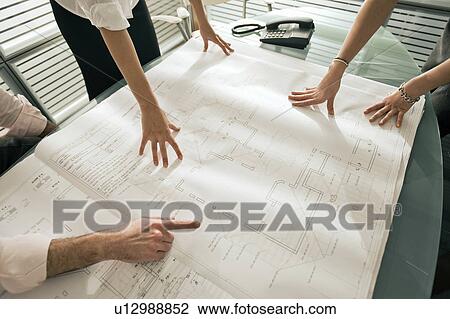 Stock Image - Closeup of professionals looking at architectural plans on desk. Fotosearch