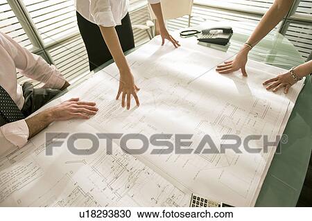 Stock Image - Closeup of professionals looking at architectural plans on desk. Fotosearch