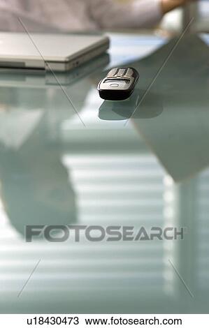 Stock Image - "Desk with laptop, cell phone, and reflection of professional woman with newspaper". Fotosearch
