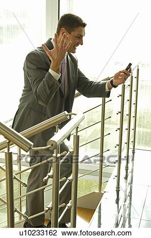 Stock Image - Happy businessman on staircase looking at cell phone. Fotosearch