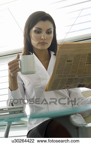 Stock Image - Professional woman reading newspaper and drinking coffee. Fotosearch