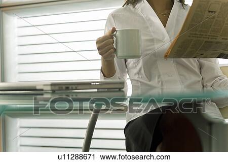 Stock Image - Professional woman with newspaper and coffee cup. Fotosearch