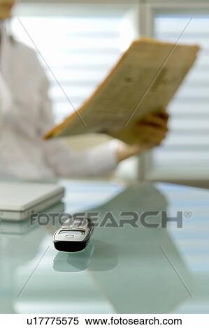 Stock Photography - Professional woman with newspaper at desk with cell phone and laptop. Fotosearch