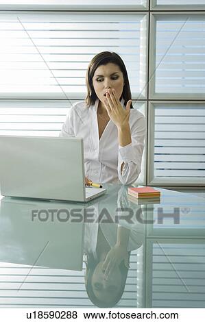 Stock Photo - Professional woman yawning at desk with laptop. Fotosearch