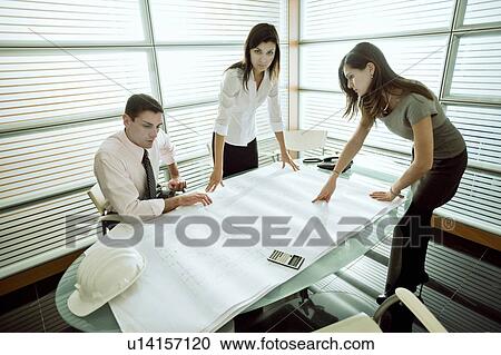 Professionals looking at architectural plans on desk View Large Photo Image Stock Image - Professionals looking at architectural plans on desk. Fotosearch