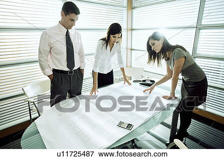 Stock Photo - Professionals looking at architectural plans on desk. Fotosearch