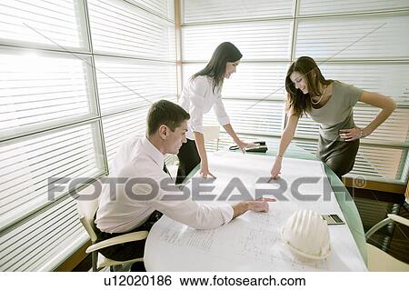 Stock Photograph - Professionals looking at architectural plans on desk. Fotosearch