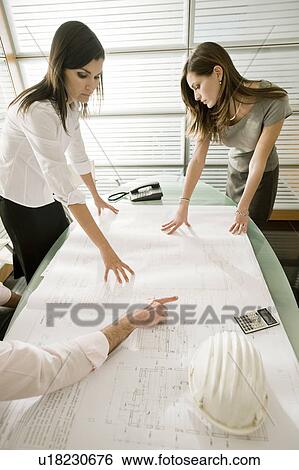Stock Photograph - Professionals looking at architectural plans on desk. Fotosearch
