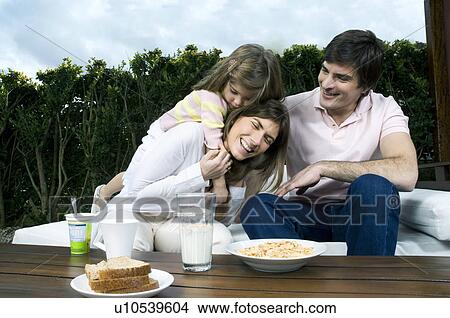 Picture - Young couple and girl having breakfast outdoors. Fotosearch