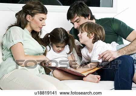 Stock Image - Young couple on couch with children reading. Fotosearch