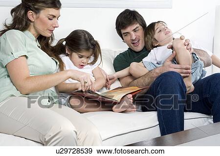 Stock Photo - Young couple on couch with children reading. Fotosearch