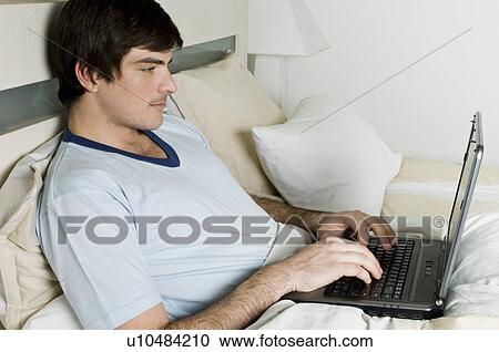 Young man in bed with laptop computer View Large Photo Image Stock Image - Young man in bed with laptop computer. Fotosearch