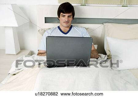 Young man in bed with laptop computer View Large Photo Image Stock Image - Young man in bed with laptop computer. Fotosearch